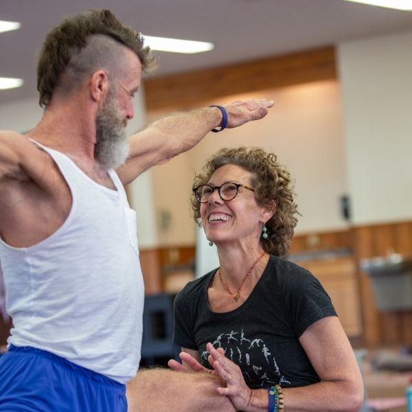 profesora de yoga anusara sonriendo y ayudando a un estudiante en pose de guerrero dos