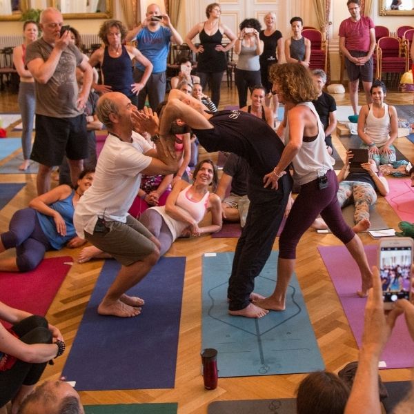 Gli insegnanti di yoga Anusara in Italia assistono uno studente in un calo in piedi mentre esprime la filosofia attraverso l'incarnazione