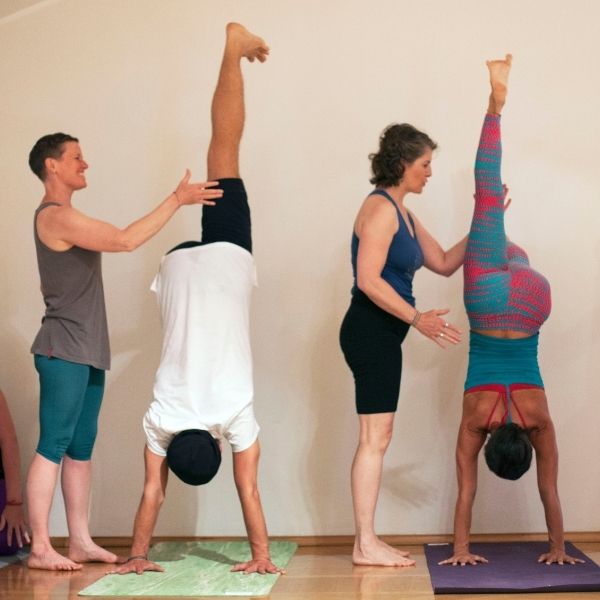 anusara yogadocenten Kim Friedman en Nicole Damen helpen studenten in handstand aan de muur in Italië