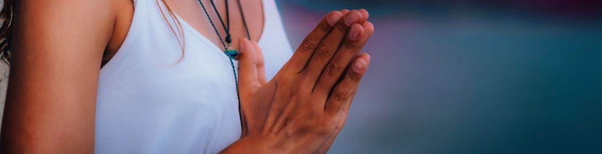 a woman with hands in prayer position, anjali mudra, preparing to chant the anusara invocation